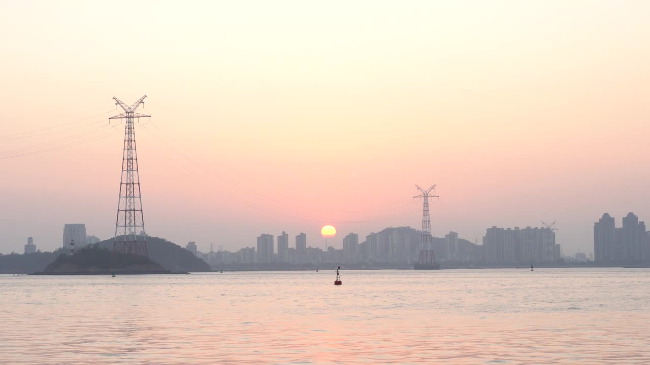 夕阳西下的海滨城市，前景是海上的高压输电塔视频素材