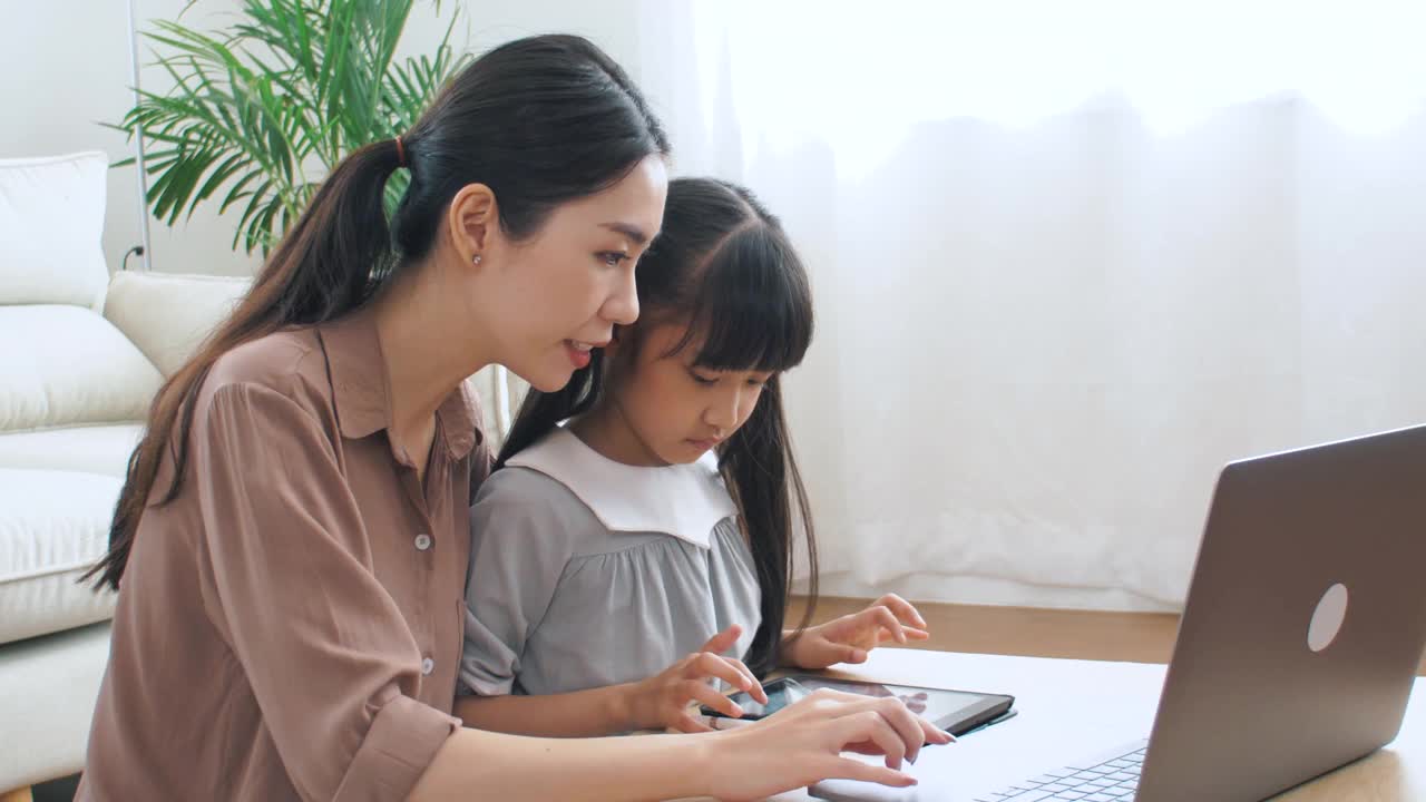 亚洲家庭与女儿学习在笔记本电脑和妈妈在客厅视频素材