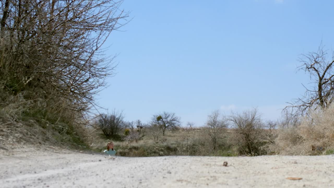 低角度观察孤独的少女走在尘土小路上，在沙漠山谷中四处张望。十几岁的女孩醒来独自在土路的相机视频素材