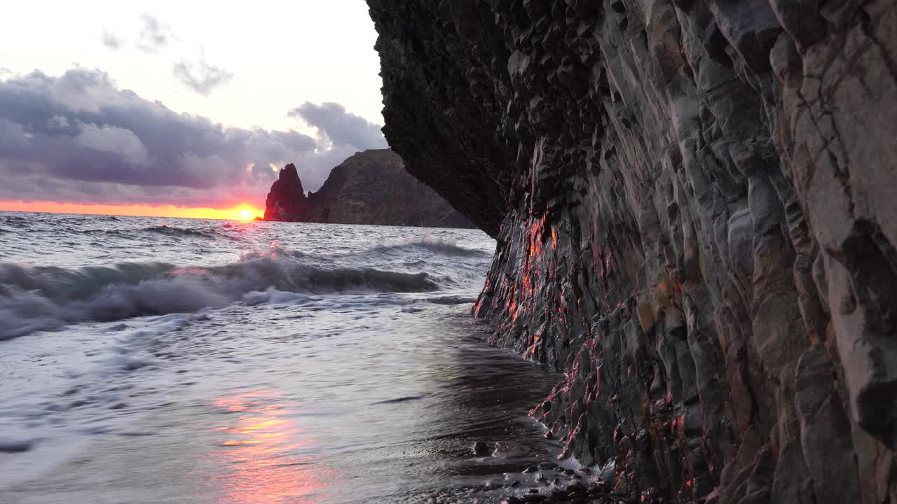 多彩的温暖的日落在海上和火山玄武岩，就像在冰岛。海浪冲击着岩石，在温暖的落日的照耀下，浪花飞溅，浪花翻滚。永恒的自然之美视频素材