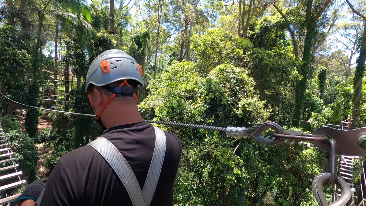 在澳大利亚阳光海岸一处林木繁茂的冒险公园里，一位健康的中年男子伸手跨上高高的秋千桥。视频素材