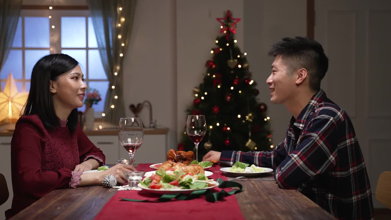 从侧面看，亚洲情侣在温馨的家中，边吃圣诞大餐边谈心视频素材