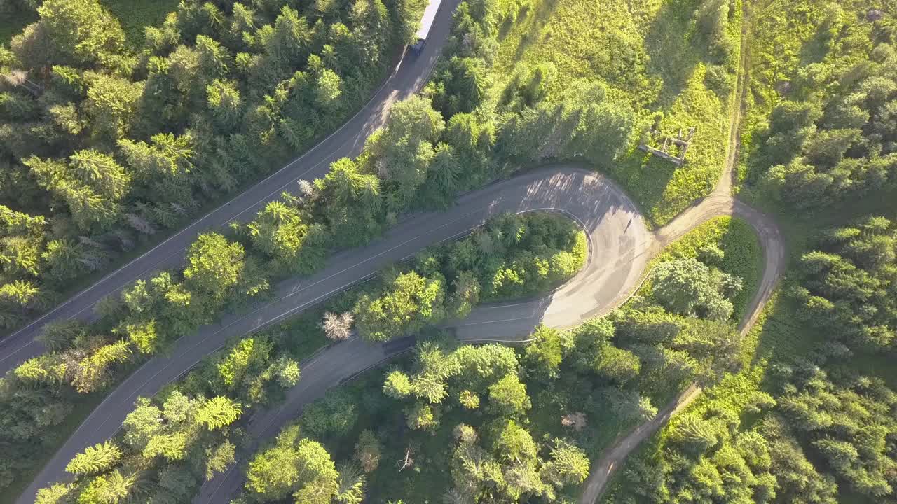 鸟瞰图蜿蜒的道路与割草汽车和卡车在高山上通过密林。视频素材