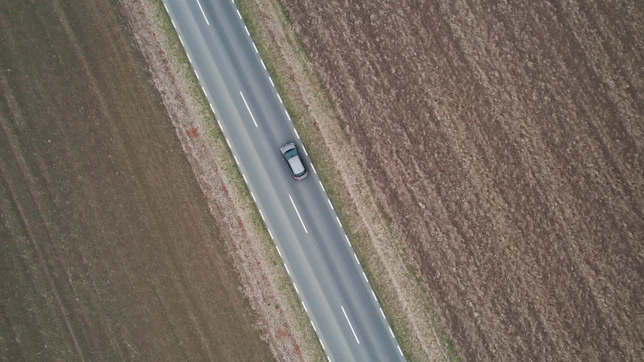 这辆车正行驶在穿过田野的道路上，无人机拍摄了航拍画面。秋天的时候在柏油路上，摄影机跟在车的后面。视频素材