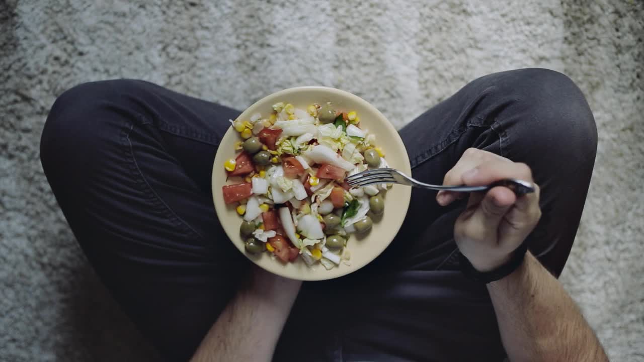 健康素食早餐，包含生菜，西红柿，玉米，橄榄。男人拿着盘子和沙拉，俯视图。清洁饮食、节食、纯素饮食理念视频素材