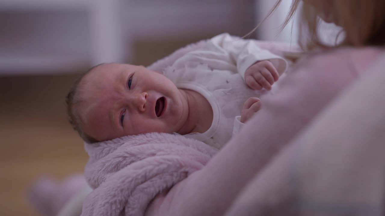 哭泣的白人新生女婴的肖像，在手中的无法辨认的母亲摇晃婴儿爱抚脸颊平静下来的女儿。多动的孩子和居家不安分的女人。视频素材