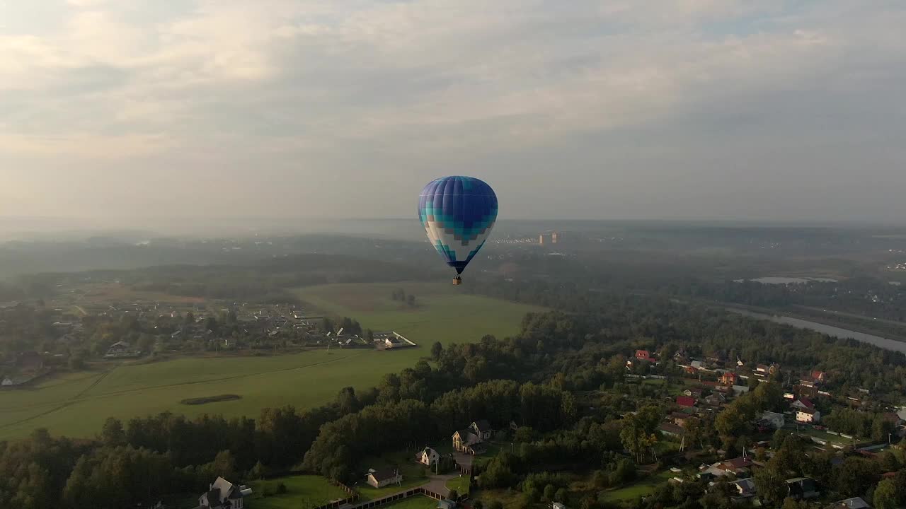 高空彩色气球在日落时飞越绿色森林的鸟瞰图。跟踪无人机飞行视频素材