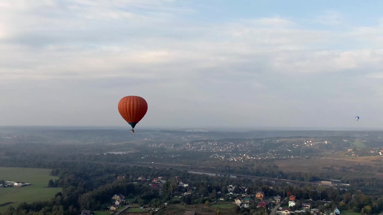 高空彩色气球在日落时飞越绿色森林的鸟瞰图。跟踪无人机飞行视频下载