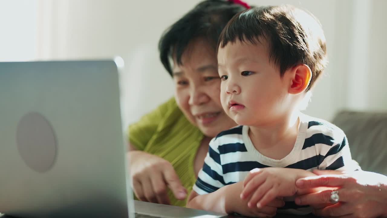 小儿子和奶奶在笔记本电脑上玩视频剪辑。视频素材