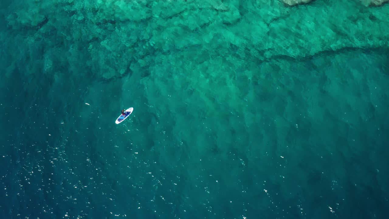 运动员驾着SUP冲浪板沿着海岩滩水域航行视频素材