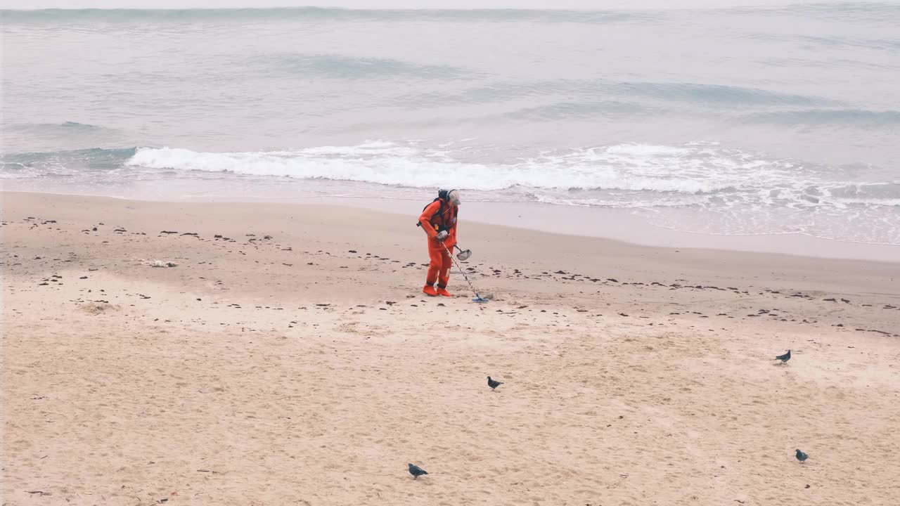 一个阴天的秋天，一名男子正在海滩上用电子金属探测器寻找丢失的奢侈品。慢镜头,4 k视频素材