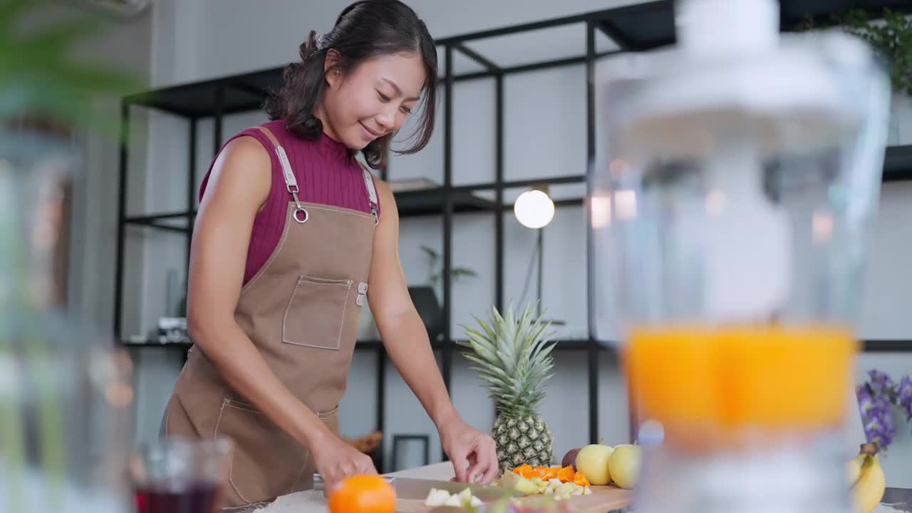 近亚洲女性穿着休闲布与围裙手切新鲜水果在木制砧板上准备奶昔水果冰沙，健康饮食生活方式亚洲女性制作水果冰沙为早上的早餐呆在家里视频素材