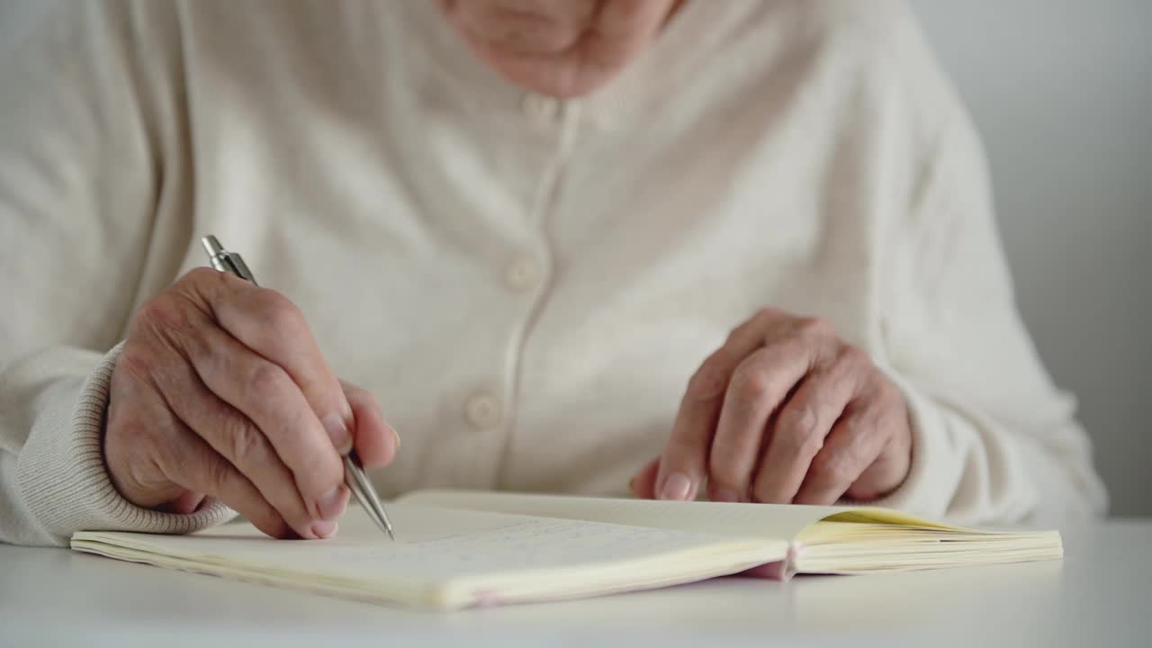 老妇人用颤抖的手写着笔记，摘下眼镜视频素材
