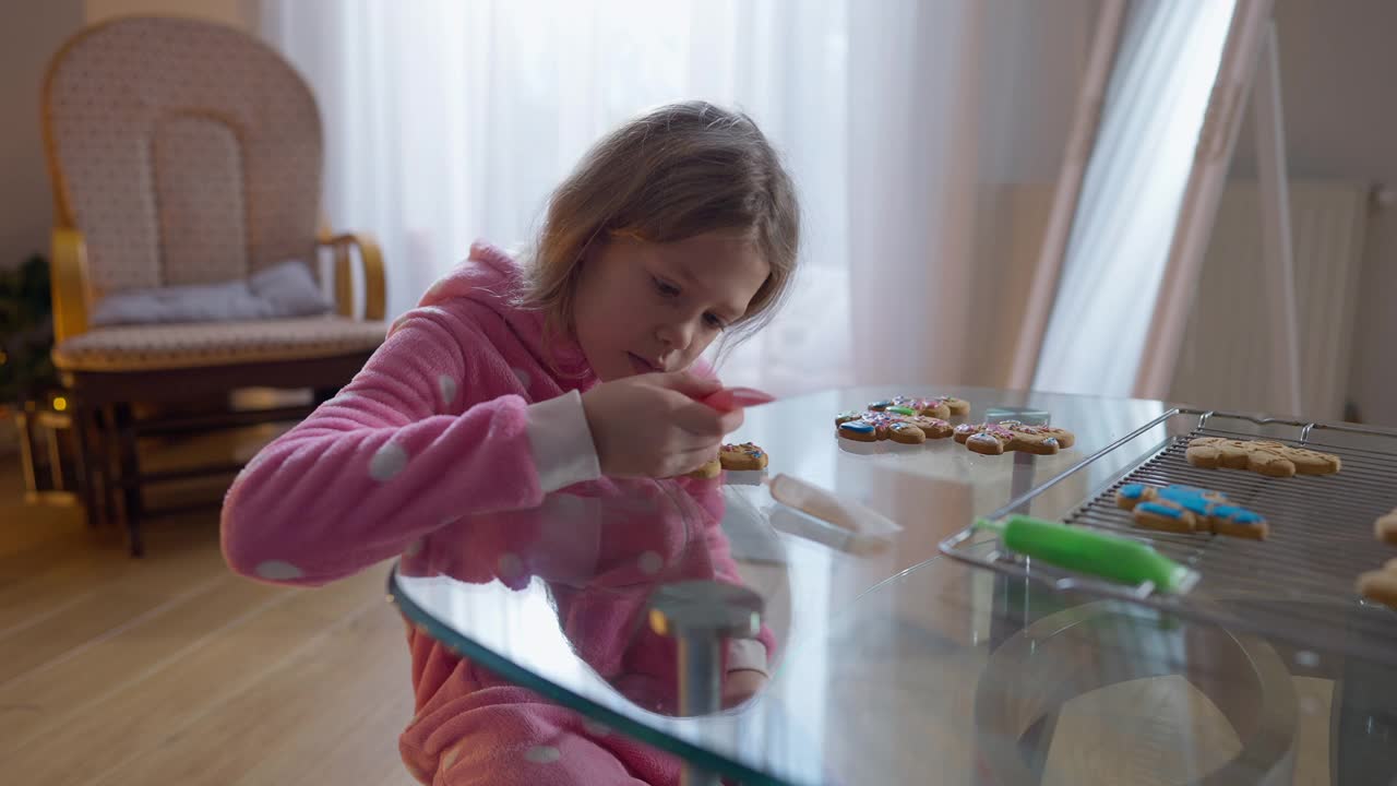 新年前夕，一个微笑的白人女孩在家里品尝着皇家糖霜装饰的传统姜饼圣诞饼干。积极无忧无虑的孩子在室内享受假期准备。视频素材