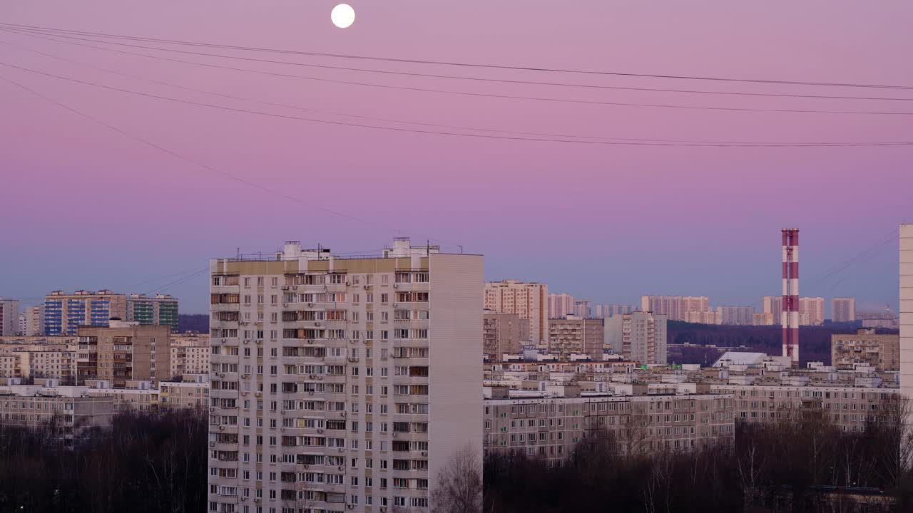 在城市景观和一根高大的红白管道的背景下，月亮在地平线上缓缓落下视频素材