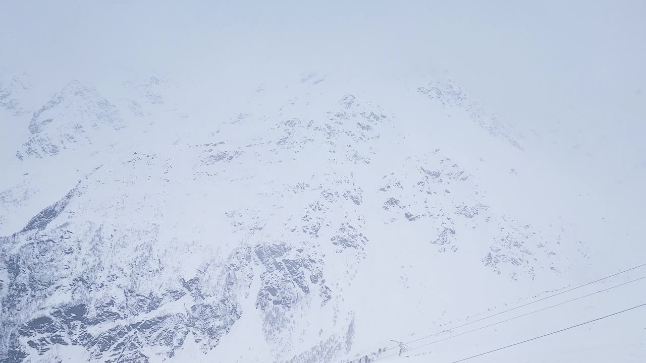 缓慢的运动。无人驾驶飞机射击。在多风的雪天，积雪覆盖的山峰的俯视图视频素材