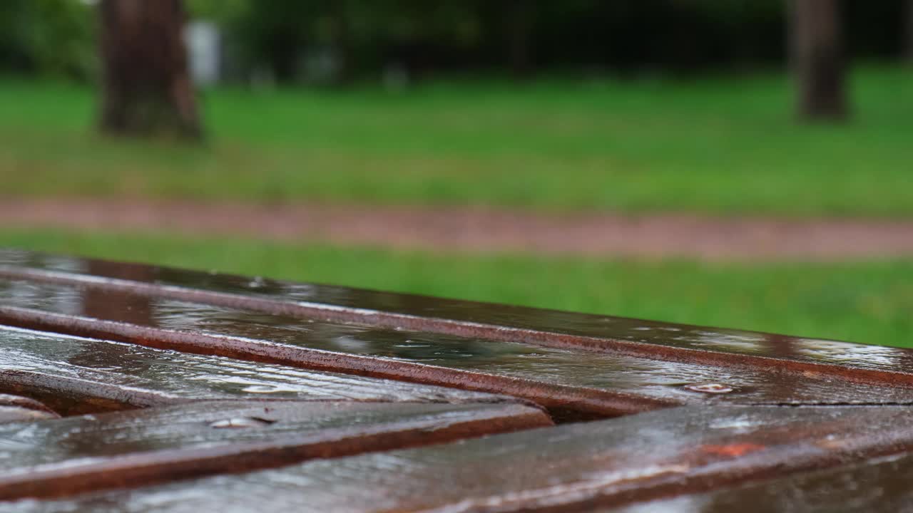 雨淋湿了公园里的长椅。多雨的天气。雨中的木椅。潮湿的城市家具。雨滴落在木凳上视频素材