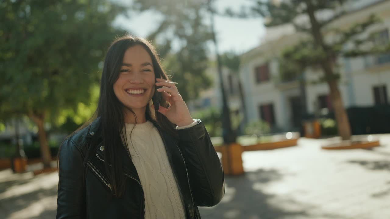 年轻的西班牙裔女性微笑自信地在公园里用智能手机说话视频素材