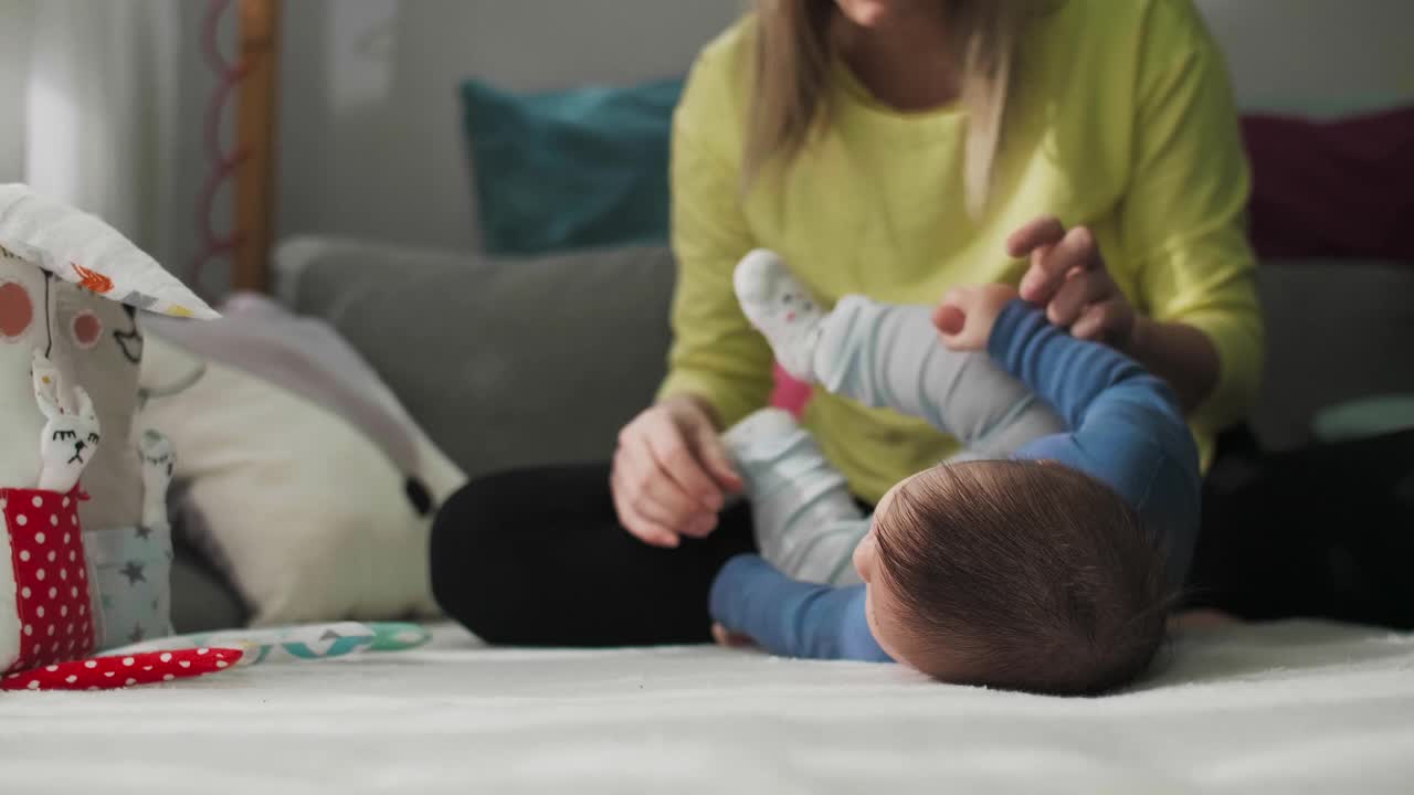 妈妈带着宝宝在客厅的沙发上锻炼，帮他俯卧翻身。视频素材