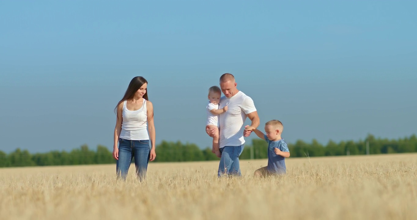 友好的一家人走在麦田里。年轻的父亲抱着一个小女儿，牵着儿子的手，快乐的父亲。全家步行，田园风光秀丽。4 k, ProRes视频素材