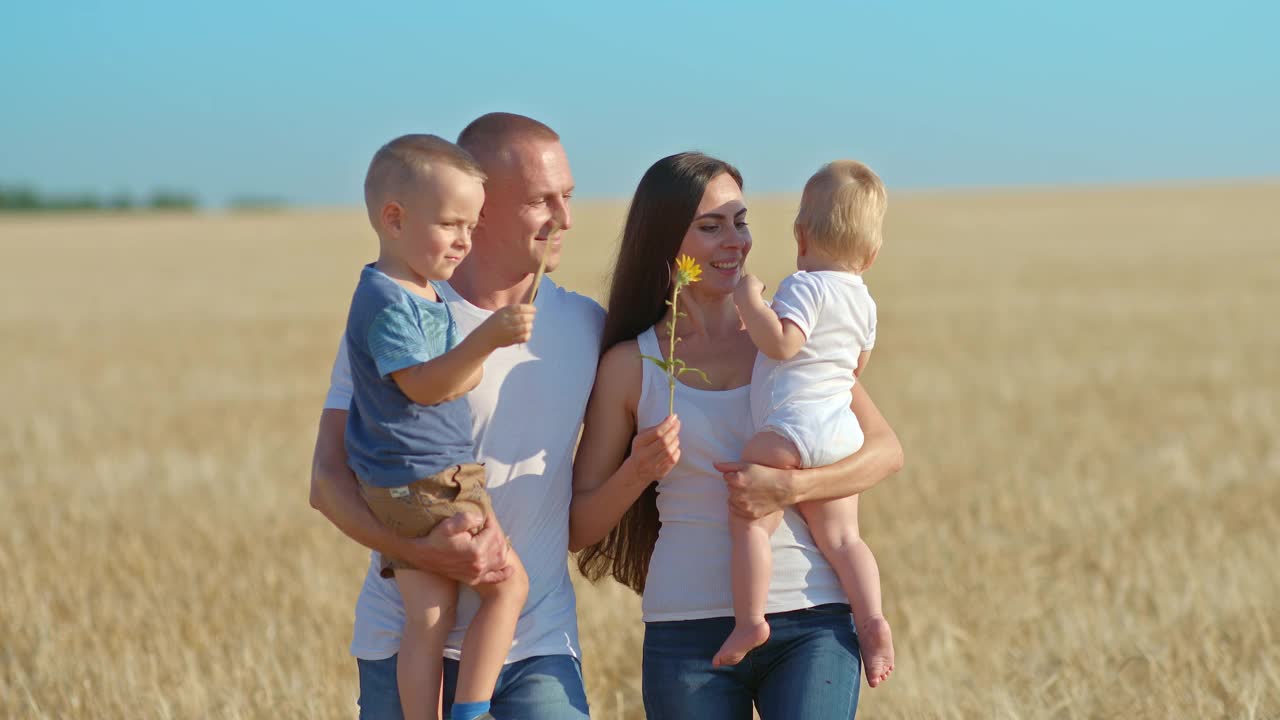 一个美丽的女人和她的家人走在麦田里。一位年轻的妇女抱着一个婴儿，微笑着，做母亲的快乐。父母抱着婴儿散步，大笑。4 k, ProRes视频素材
