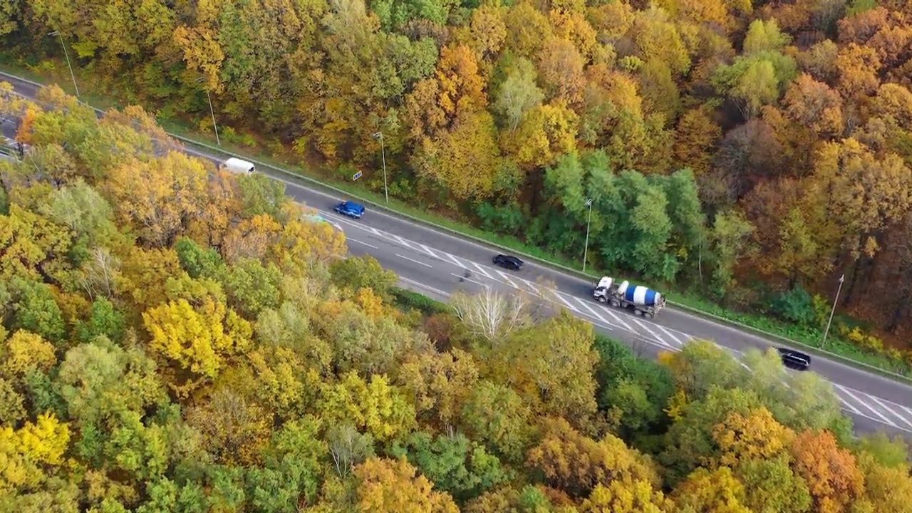 高速公路两旁有五颜六色的树木。汽车在秋天的森林中行驶。树顶和柏油路上有汽车。鸟瞰图。视频素材