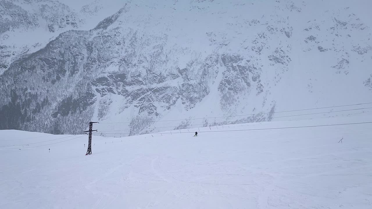 缓慢的运动。无人驾驶飞机射击。在下雪的天气里，一个孤独的滑雪者沿着山坡向下滑行的俯视图视频素材