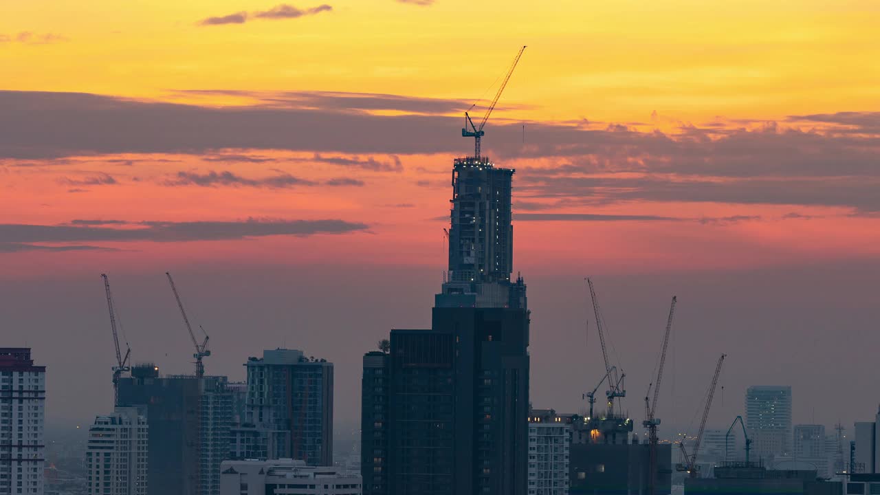 亚洲市区摩天大楼的延时拍摄，起重机工作，日落剪影的城市景观。建筑行业，工业企业，或土木工程技术概念视频素材