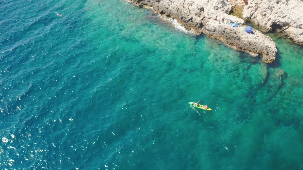 人们划着色彩鲜艳的皮划艇，沿着大海经过岩石海滩视频素材