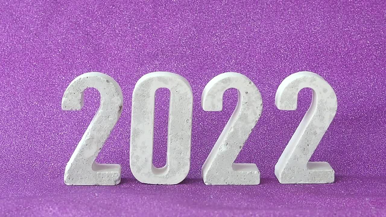 混凝土数字2022在闪亮的紫色背景上，落在他们的人造雪上。视频素材