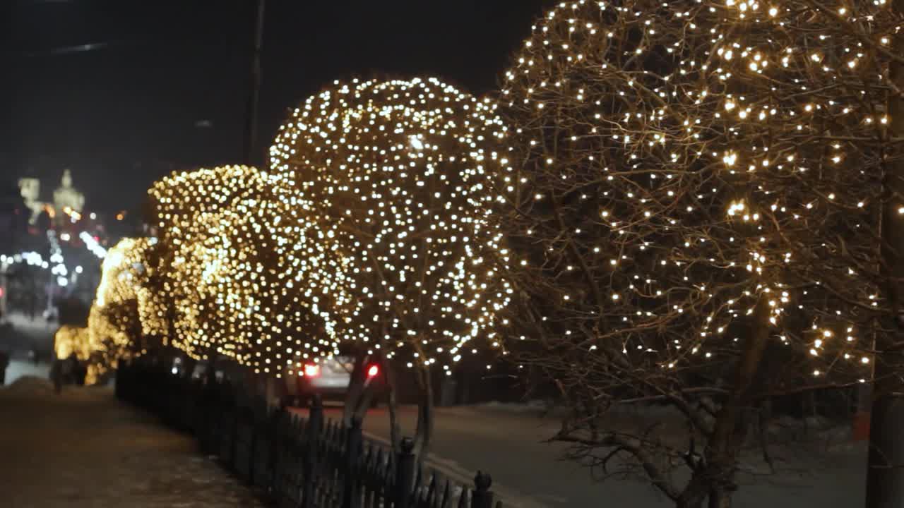 街道两旁的树上、圣诞花环灯和交通道路上的汽车上的夜间装饰照明视频下载