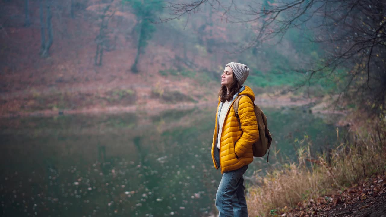 一位年轻的成年妇女站在森林湖边，深深地吸了一口气。视频素材