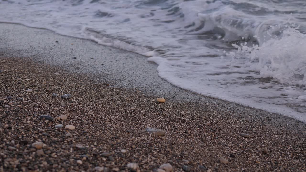 13、海滩上的卵石，翻滚的海浪带着泡沫。海景视频素材