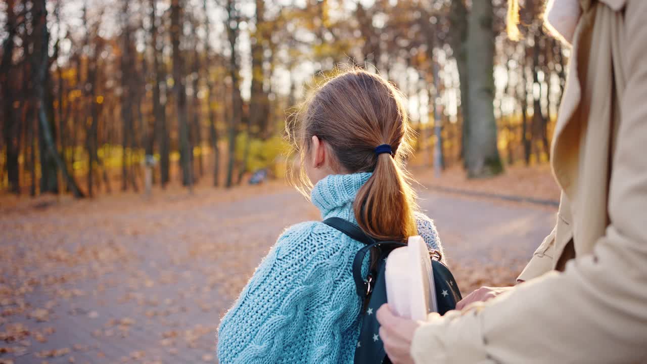 年轻的妈妈把塑料容器放进小女儿的背包里，拉上拉链。拥抱，微笑，然后一起离开。秋天,公园。近距离视频素材