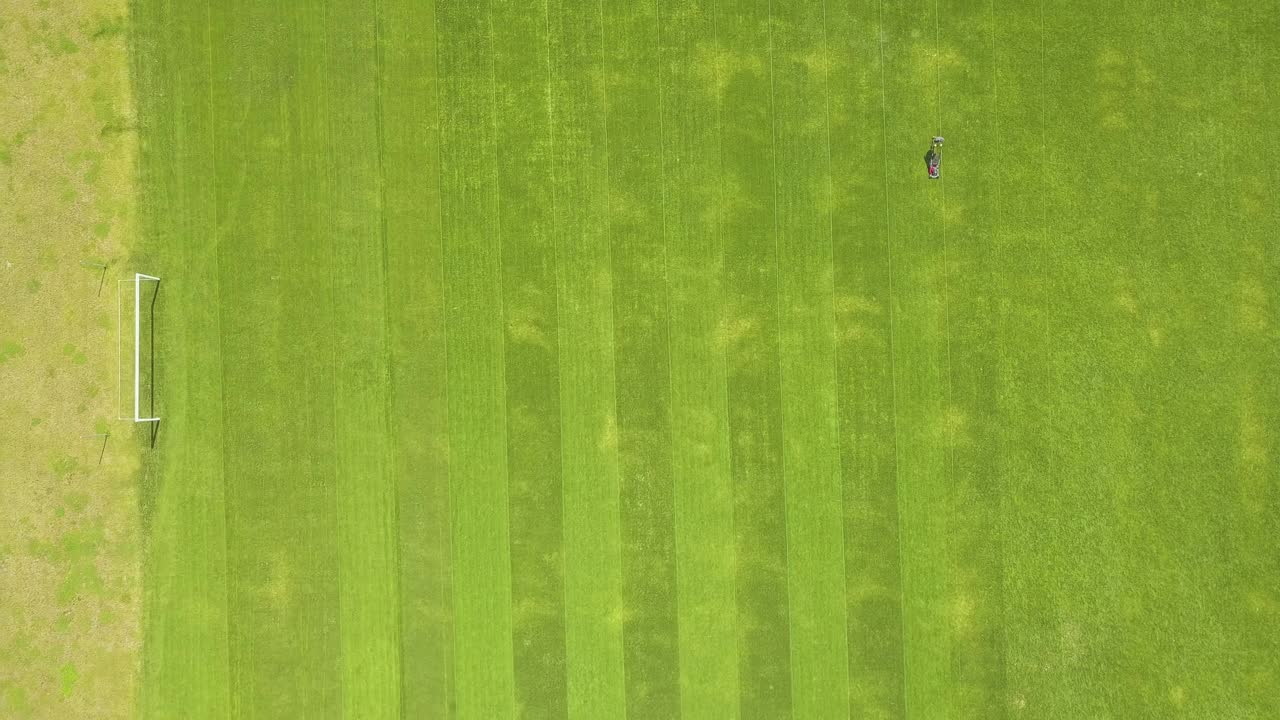 鸟瞰图:夏季足球场上用割草机修剪青草的工人的小身影视频素材