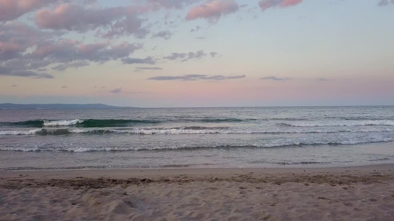 鸟瞰图的海面与蓝色的水波浪下紫色的日落天空视频素材