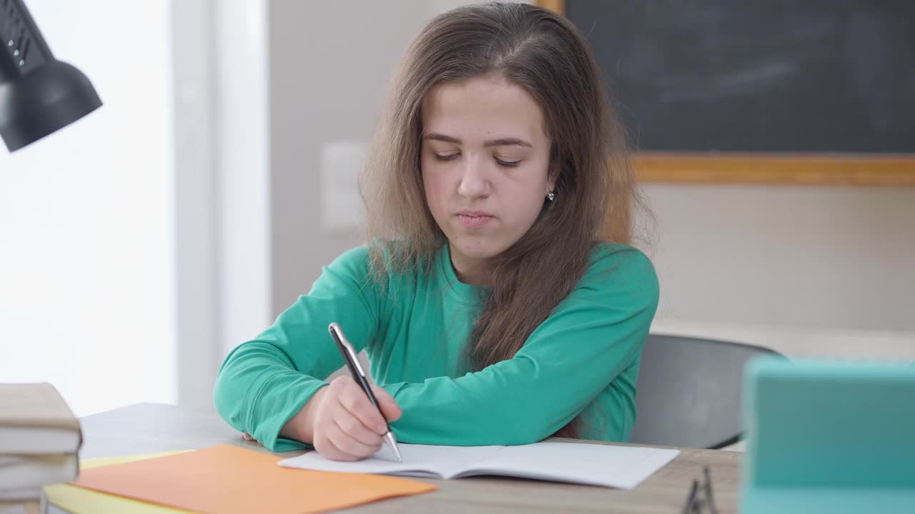 集中的白种人妇女写钢笔坐在书桌边叹息疲于研究。肖像的聪明无聊的小个子在室内学习，思考，看别处。穷尽与教育理念。视频素材