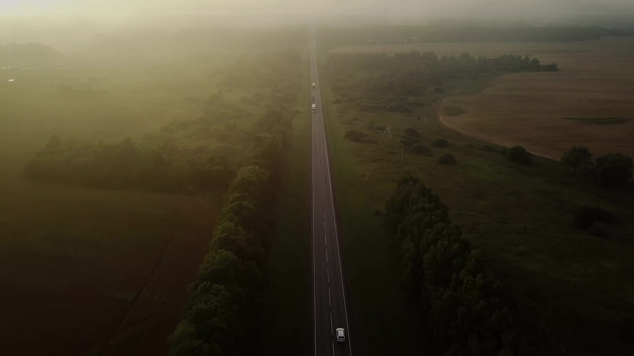 从无人机上射击。一架四轴飞行器从空中穿过云层，拍摄日落、树木、道路和汽车。令人难以置信的景色。视频素材