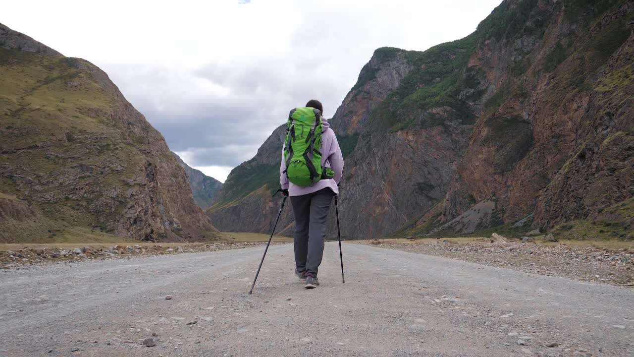 在落基山脉背景的地面道路上用登山杆徒步旅行的女人视频素材