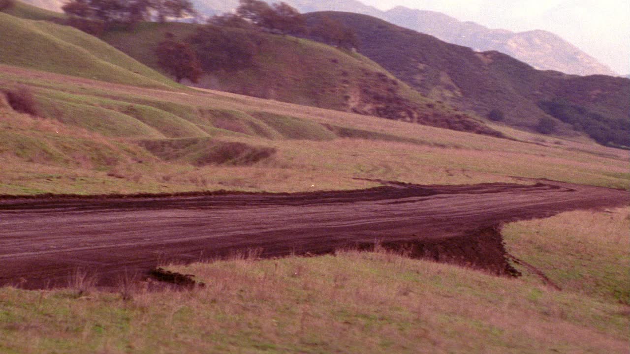 飞机从泥土跑道上起飞的空中飞行景象。飞机不可见。山脉。山。云。视频素材