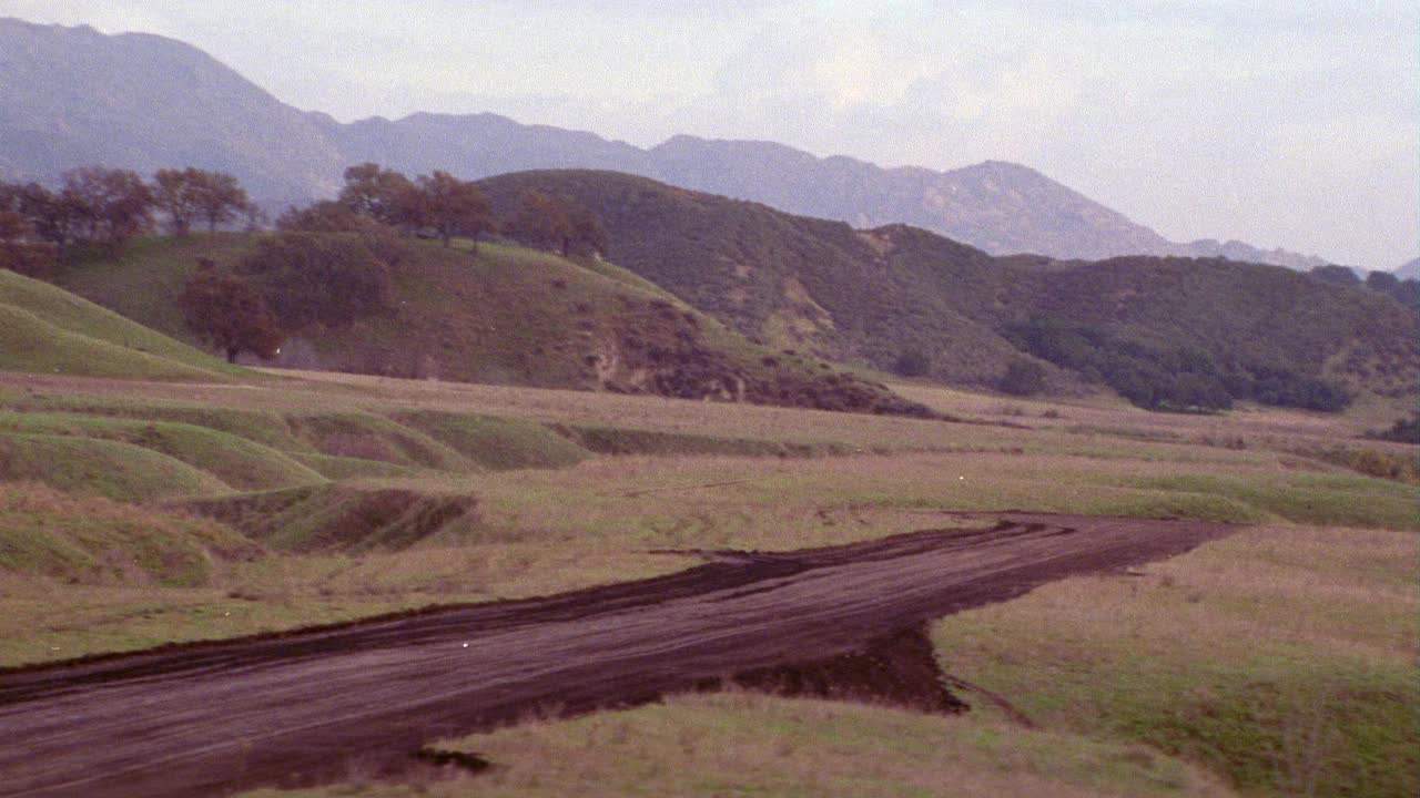 飞机从泥土跑道上起飞的空中飞行景象。飞机不可见。山脉。山。云。视频素材