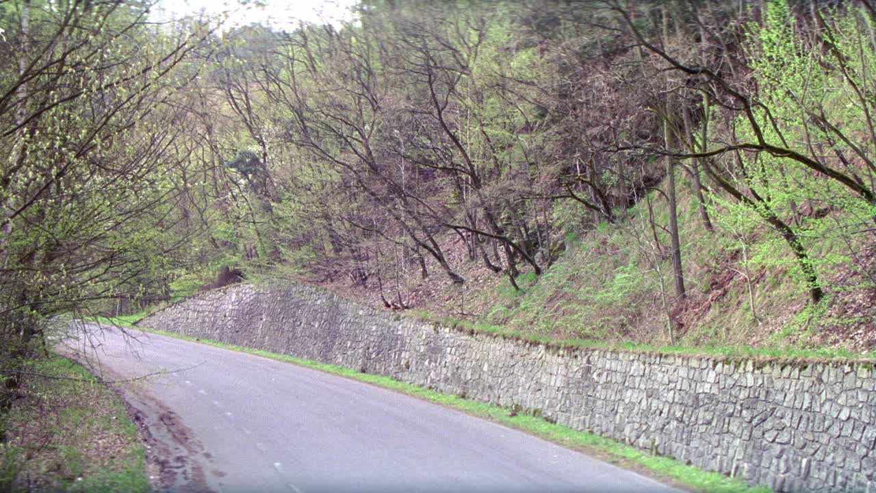 广角1967年庞蒂亚克gto肌肉车行驶在乡间道路，通过石头堤岸和森林或林区。树。视频素材