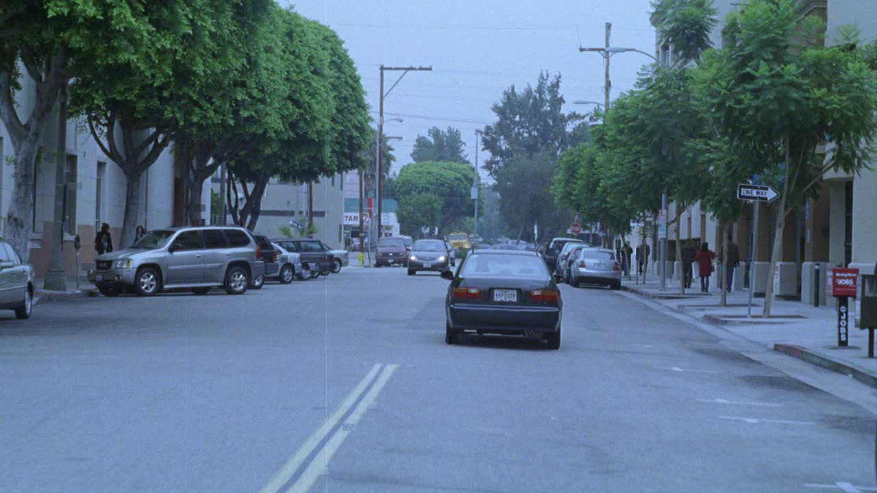 跟踪拍摄的汽车行驶在城市街道上与停车和通过的汽车。转向威尼斯大道的信号。行人在人行道上。十字路口的商业或商店和公寓楼。停止的迹象。视频素材