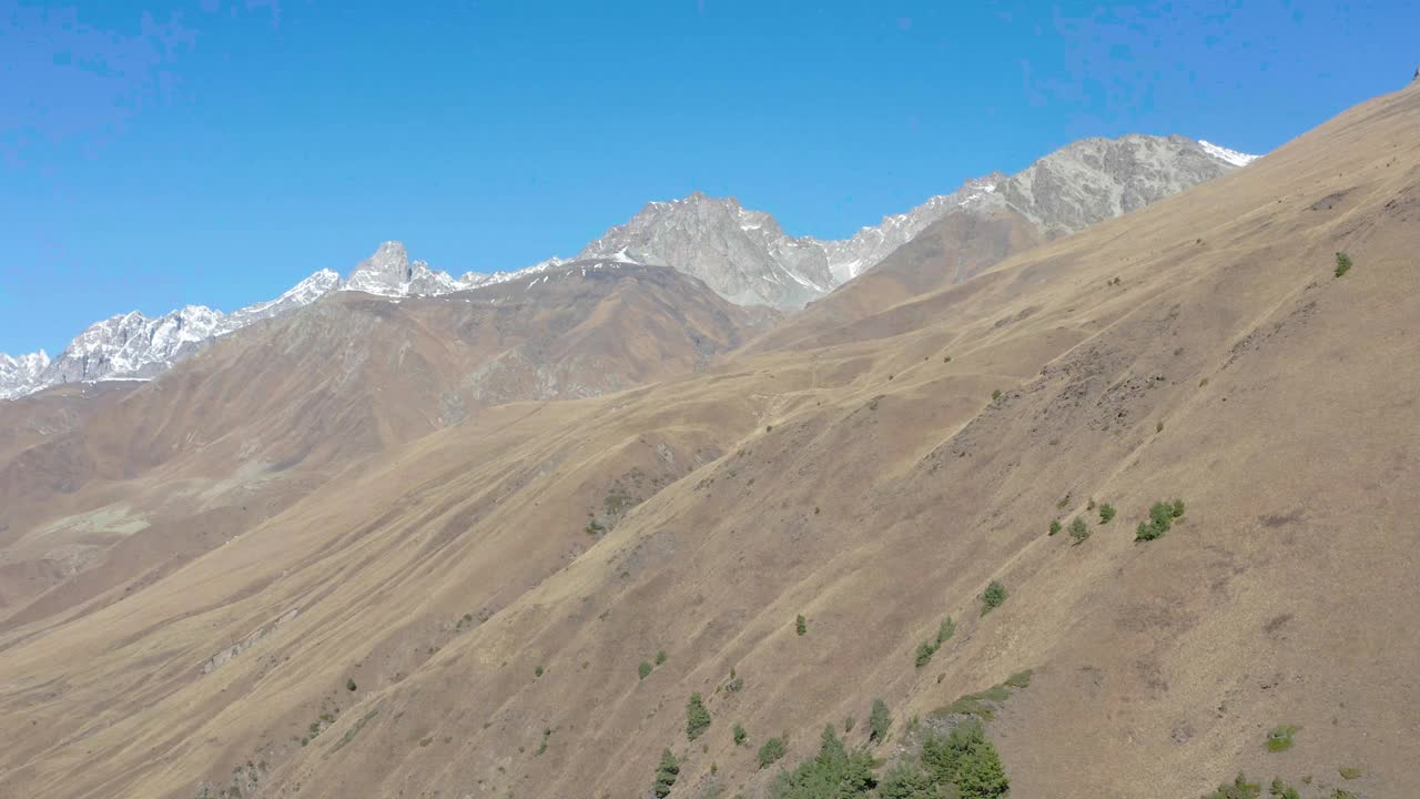 在阳光明媚的秋日，无人机沿着峡谷上方覆盖着积雪的棕色山脉飞行视频素材