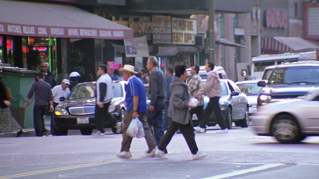 广角行人或城市街道十字路口的人行横道。汽车和警车在后面等待着。典当行和“无付款鞋源”鞋店可见。可能是较低阶层的社区，城市地区，或downt视频素材