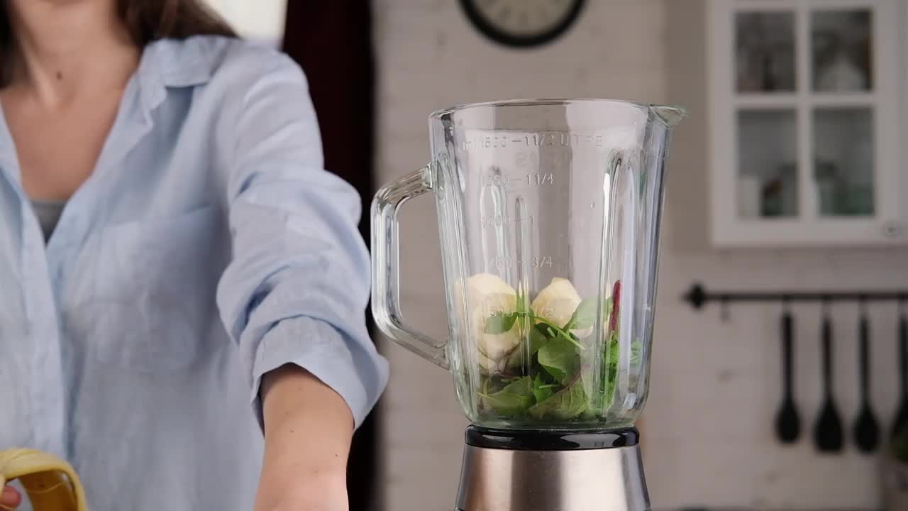 年轻女子在家制作排毒奶昔。年轻女子正在用香蕉、菠菜和芝麻菜做绿色奶昔。视频素材