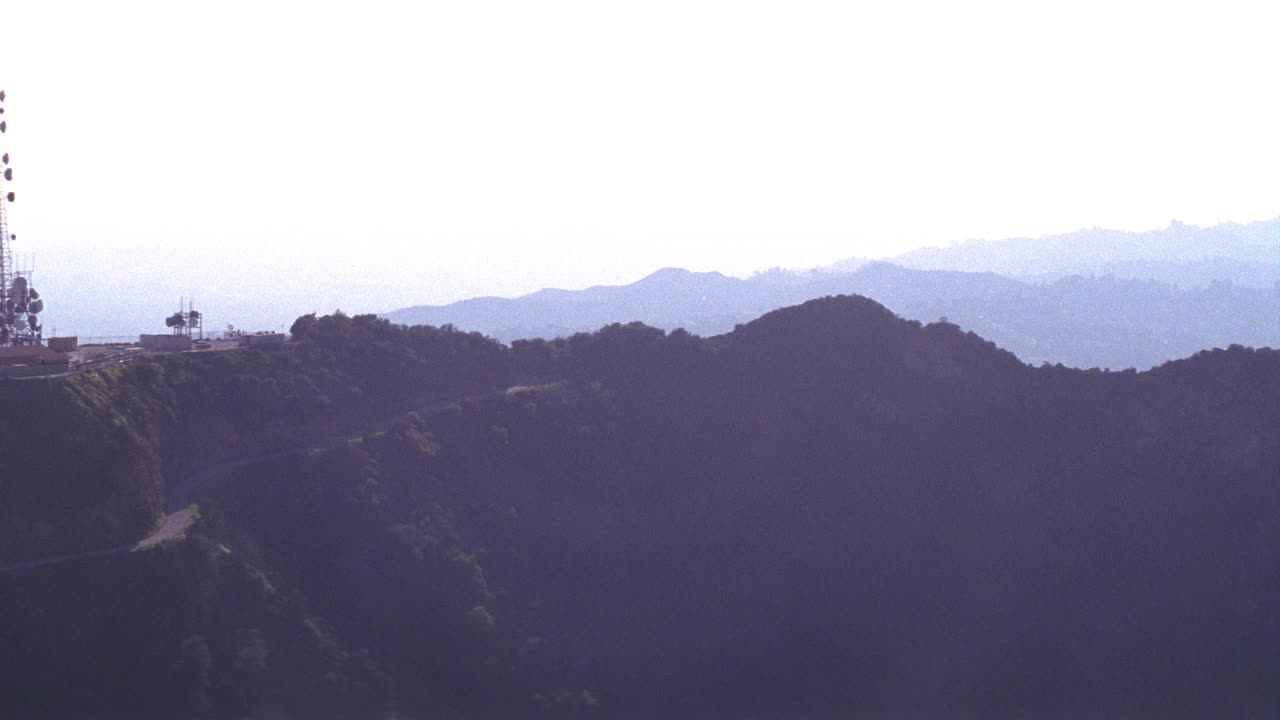 在“好莱坞”标志的山顶架空，安装无线电天线塔。市区天际线与烟雾和阴霾的地平线。视频素材