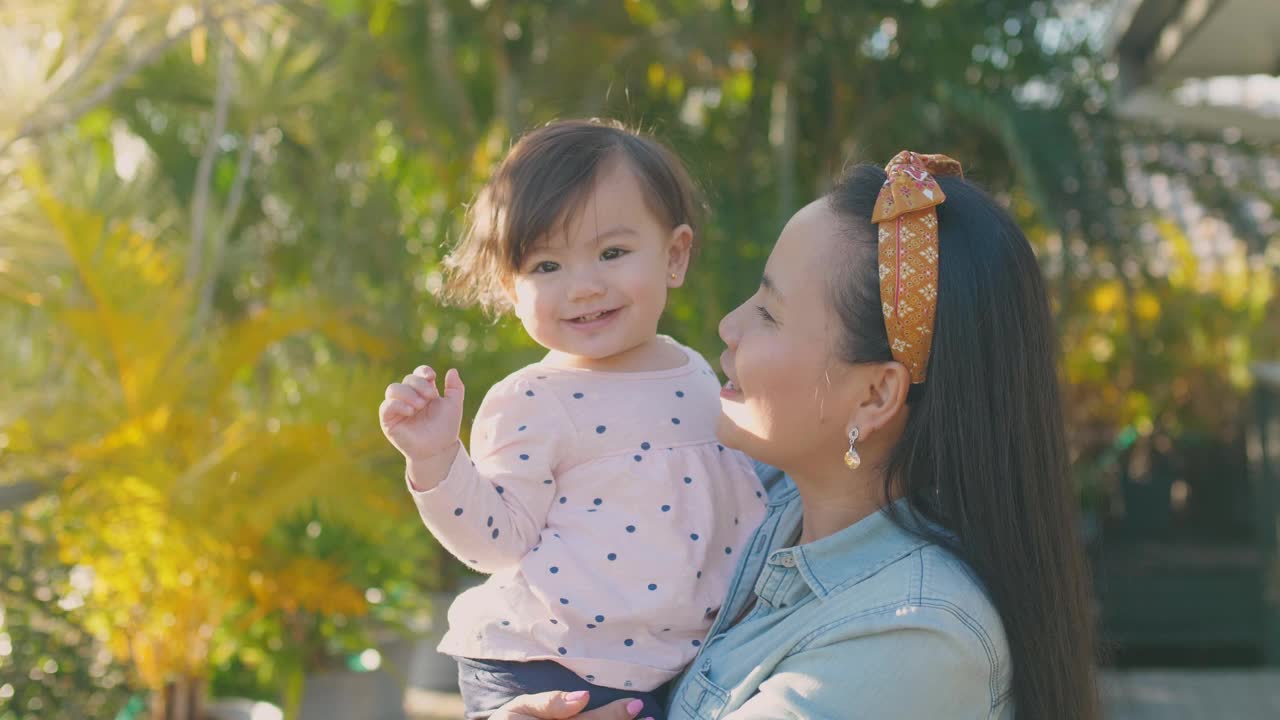 亚洲母亲亲吻她的多民族蹒跚学步的女儿的肖像，家庭爱的概念视频素材