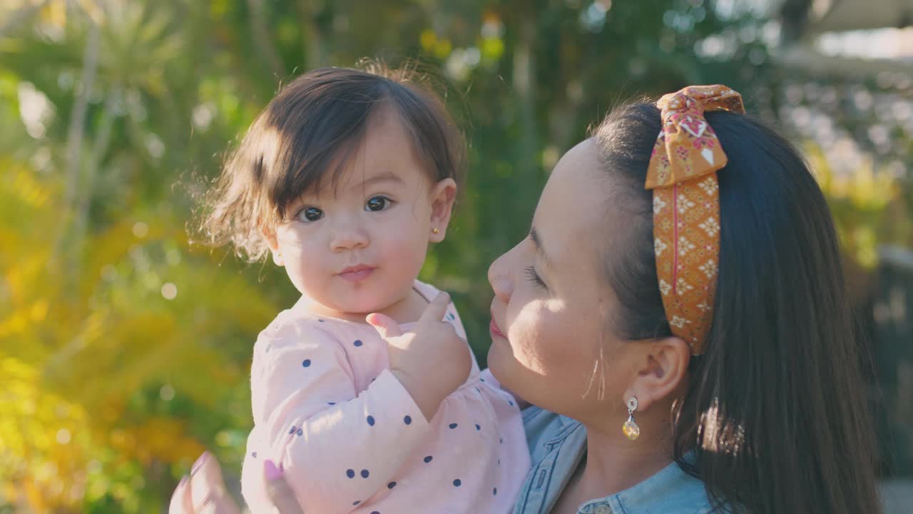 亚洲母亲亲吻她的多民族蹒跚学步的女儿的肖像，家庭爱的概念视频素材