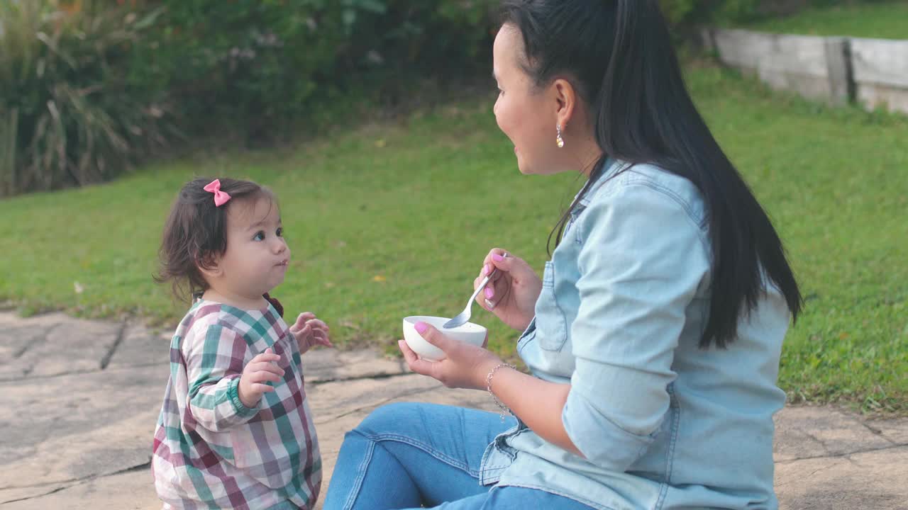 亚洲母亲在前院喂养她的混合蹒跚学步的女儿，家庭生活理念视频素材